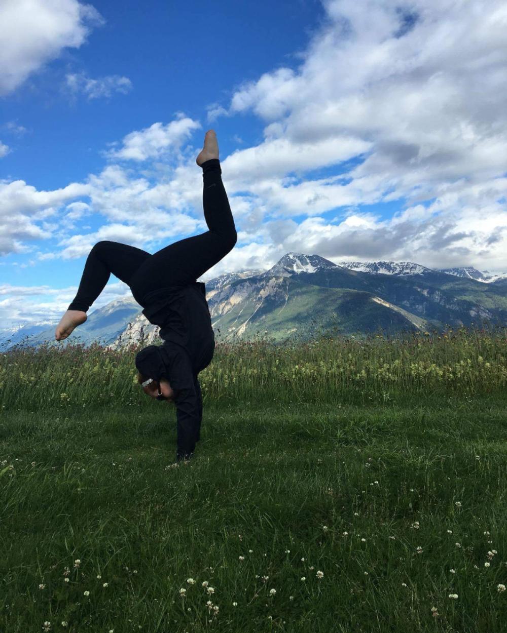 Student doing a handstand in a field with a mountain in the background